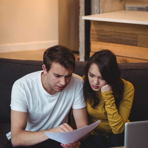 Couple sitting on sofa discussing with financial documents in living room at home